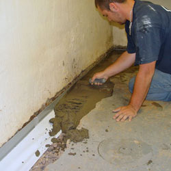 A contractor in Sacramento installing a perimeter drain tile system during a sump pump installation.